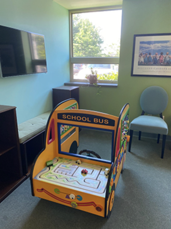 Children’s play area with a wooden school bus activity table and a wall-mounted TV